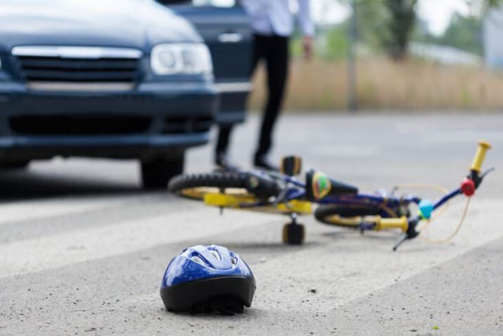 After a car accident: a blue helmet lies on the crosswalk, while a mangled bicycle rests in the background near a car and its driver.